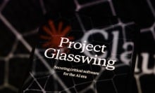 The visual for Project Glasswing is displayed on a smartphone screen placed on a reflective surface onto which a Claude logo with hexagonal patterns is projected