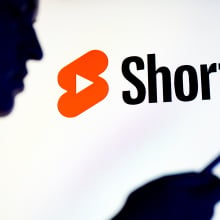 A person stands in profile staring at a phone. A large YouTube Shorts logo glows behind them. 