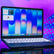 indigo macbook neo opened to home screen in front of purple background