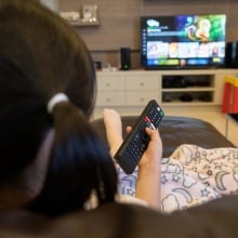 A young girl watches TV with remote in her hand.