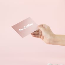 Hand holding a pink invitation card on pink background.