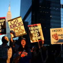 A group of protesters, some wearing Knicks jerseys, hold up anti-Trump signs outside MSG.