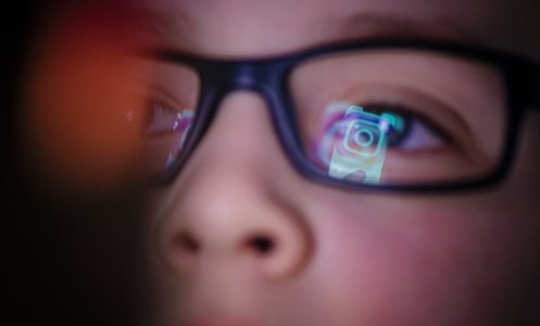 Instagram logo is reflected in boy's glasses. 