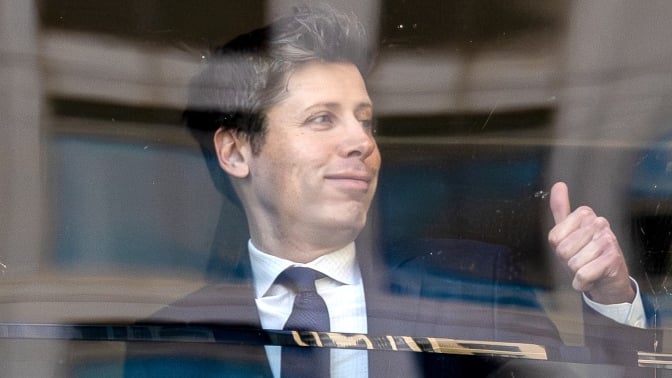 Sam Altman gives the thumbs-up behind glass