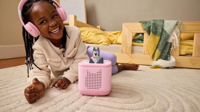 girl wearing headphones on rug with Bluey toniebox