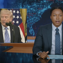 A man sits behind a talk show desk. In the top left is an image of the president.